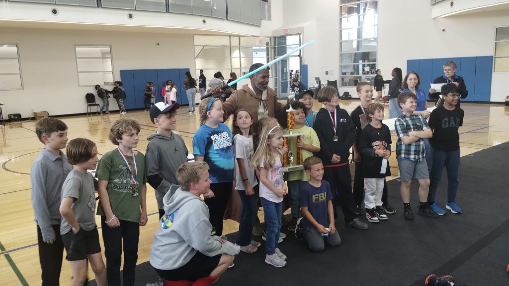 players pose with Martial Arts academy instructor and his light saber at the 2024 Seven Cities School Chess Championship